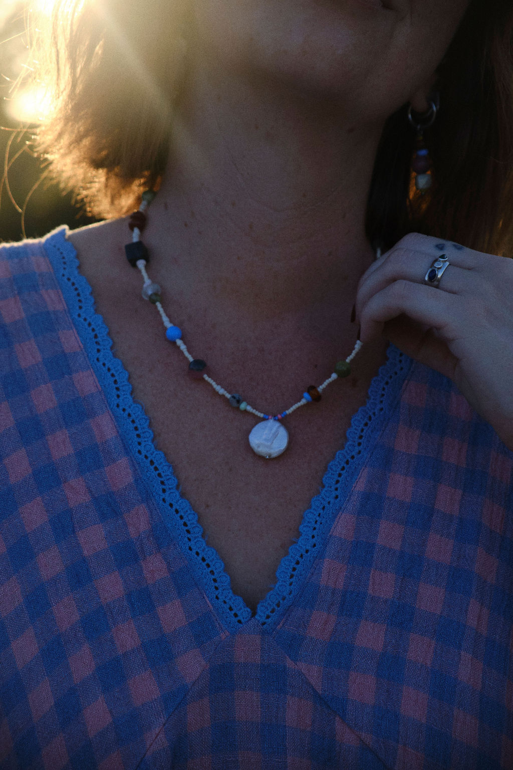 Amilita Haze Necklace – close-up of handmade beaded necklace with a round shell pendant, worn with a blue and pink gingham dress